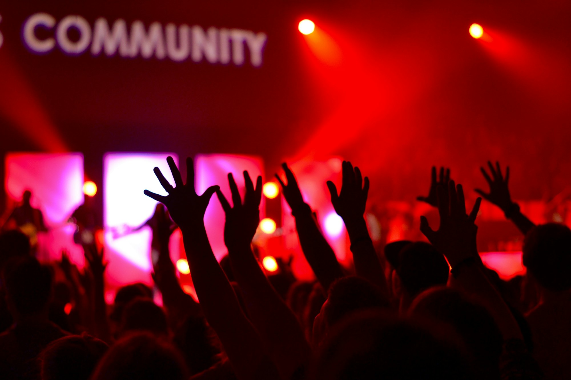 People raising their hands in front of a band on stage. There is a 'Community' written at the top