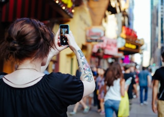 focus photo of woman in black cap-sleeved shirt holding smartphone while taking photo