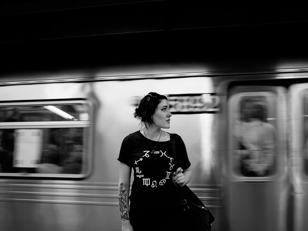 grayscale photography of woman standing near train