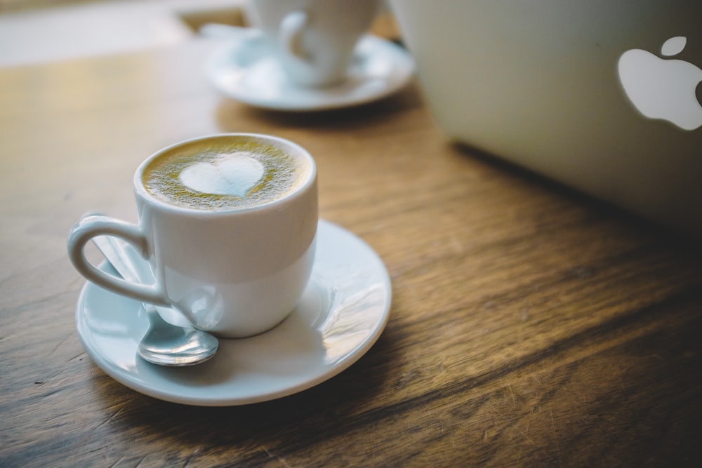 weiße Keramiktasse mit Untertasse auf braunem Holztisch