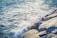 Waves crash against a rocky shoreline with water spraying upwards, creating a dynamic interaction between the ocean and the rocks.