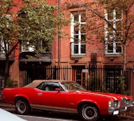 A classic red convertible parked on a cobblestone street under autumn leaves.