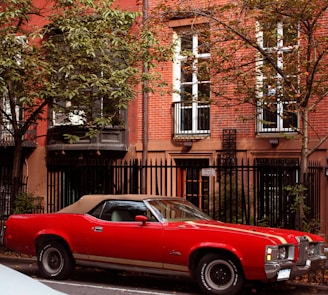 A classic red convertible parked on a cobblestone street under autumn leaves.