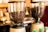 Two coffee grinders filled with dark roasted coffee beans, standing on a counter. The background is blurred, creating a warm and inviting atmosphere typical of a coffee shop.