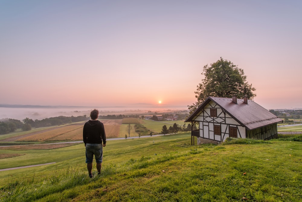 man standing near house and tree at daytime