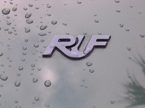 A glossy emblem displays the letters 'RUF' against a green metallic surface dotted with water droplets, indicating a recent rain or a moist environment.