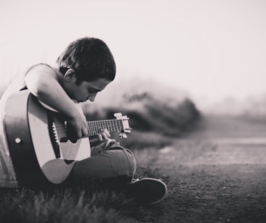 grayscaled photo of boy playing guitar