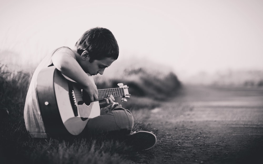 grayscaled photo of boy playing guitar