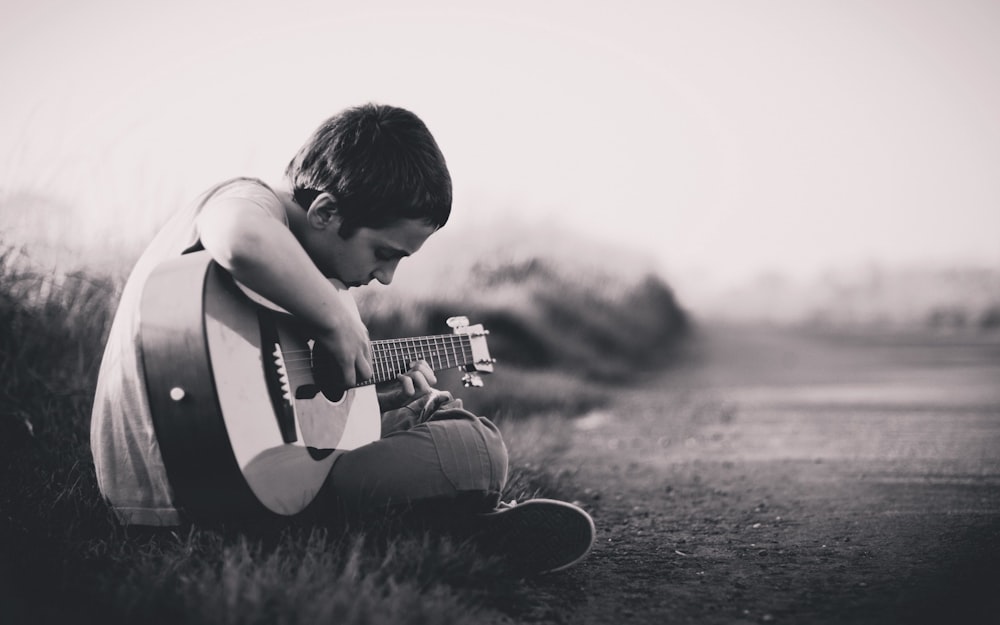 기타를 연주하는 소년의 회색조 사진