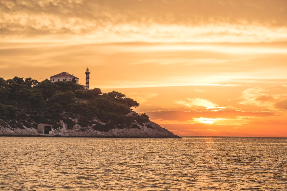 silhouette of lighthouse on top of hill during sunset