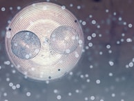 A circular design with concentric rings, accompanied by two smaller circles that create an abstract appearance. There are light orbs scattered across, giving a dreamy or mystical effect.
