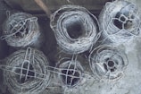 Rows of barbed wire rolls stacked neatly in a spacious factory warehouse with blue steel beams.