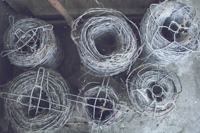 Rows of barbed wire rolls stacked neatly in a spacious factory warehouse with blue steel beams.