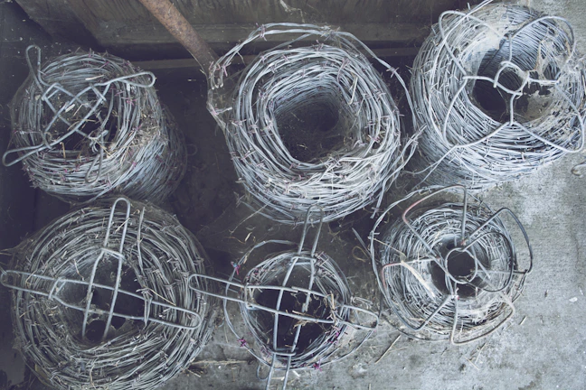 Rolls of concertina wire ready for installation, stacked neatly in a warehouse with green military accents.