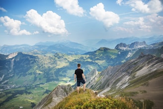 A serene landscape with a person standing on a mountain peak, looking out over a vast horizon.