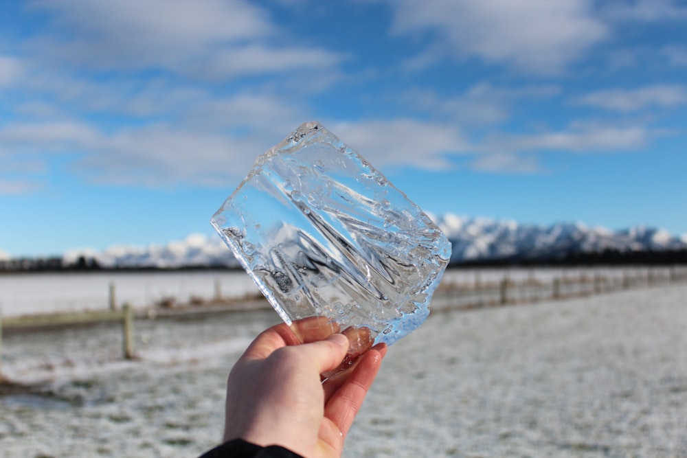 person holding clear shard under blue sky