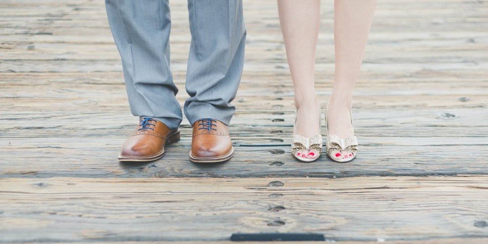 homem vestindo sapatos oxford de couro marrom ao lado da mulher usando sandálias de ouro de dedo aberto