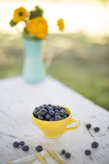 Steaming cup of blueberry tea with fresh berries and farm greenery blurred in the background