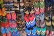 A colorful array of various flip-flops and sandals hanging on display. They feature multiple designs and patterns, including floral prints, stripes, and logos in a vibrant mix of colors like red, blue, green, and pink.