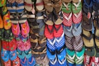 A colorful array of various flip-flops and sandals hanging on display. They feature multiple designs and patterns, including floral prints, stripes, and logos in a vibrant mix of colors like red, blue, green, and pink.