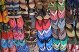 A colorful array of various flip-flops and sandals hanging on display. They feature multiple designs and patterns, including floral prints, stripes, and logos in a vibrant mix of colors like red, blue, green, and pink.