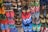 A colorful array of various flip-flops and sandals hanging on display. They feature multiple designs and patterns, including floral prints, stripes, and logos in a vibrant mix of colors like red, blue, green, and pink.