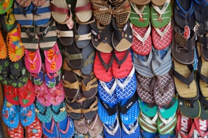 A colorful array of various flip-flops and sandals hanging on display. They feature multiple designs and patterns, including floral prints, stripes, and logos in a vibrant mix of colors like red, blue, green, and pink.