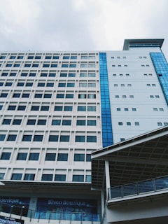 A modern multi-story building with a grid-like pattern of windows and contrasting blue glass panels. The structure appears to be part of a larger complex, with a visible sign for Bingo Boutique on the ground floor. The sky above is overcast, adding a subdued atmosphere.