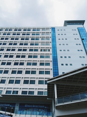A modern multi-story building with a grid-like pattern of windows and contrasting blue glass panels. The structure appears to be part of a larger complex, with a visible sign for Bingo Boutique on the ground floor. The sky above is overcast, adding a subdued atmosphere.