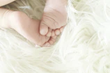A child’s small feet snug in soft cotton slippers, standing on a fluffy white rug.
