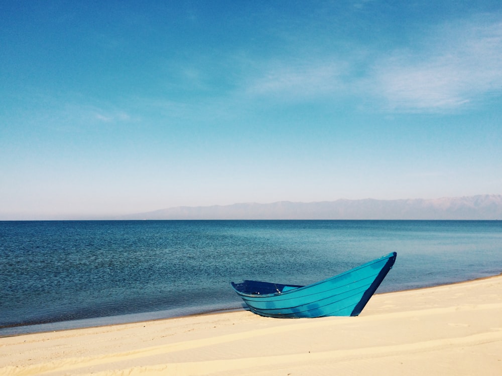 Bateau bleu sur le sable près du plan d’eau pendant la journée