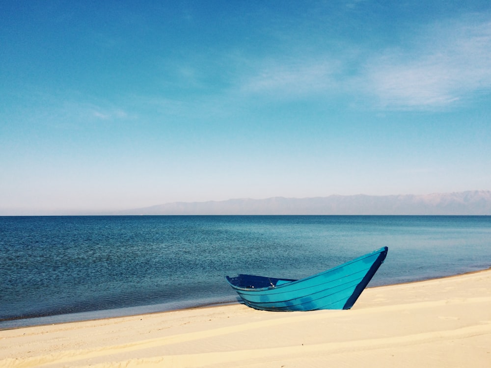 blue boat on sand near body of water during daytime