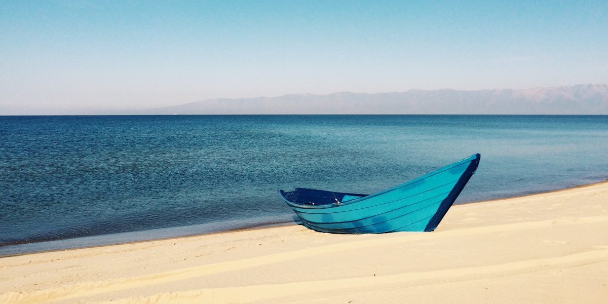 blue boat on sand near body of water during daytime