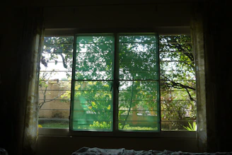 Soft olive green curtains gently flowing in natural light, framing a window with a view of greenery.