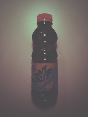 A plastic bottle with a red cap and a label indicating it contains Nestea iced tea with a peach flavor. It is placed upright against a plain background.