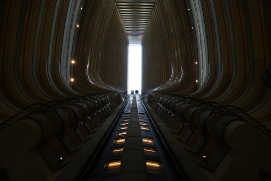 A transparent panoramic glass elevator shaft rising through a bright, open atrium with natural light.