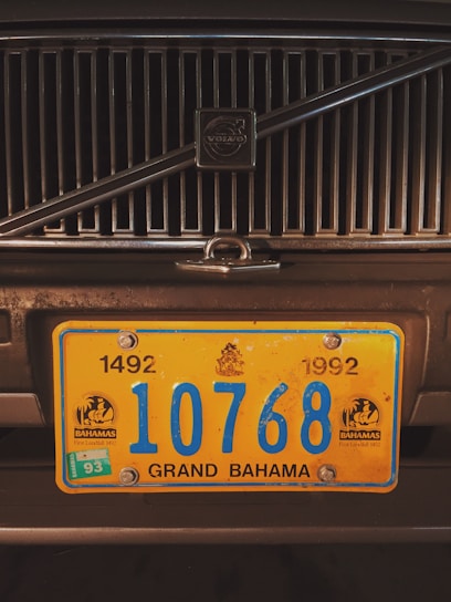 A close-up of a vehicle's front grill with a prominent yellow and blue license plate from Grand Bahama. The license plate has the number 10768 and includes the years 1492 and 1992 with emblems on either side.