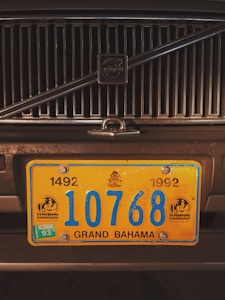 A close-up of a vehicle's front grill with a prominent yellow and blue license plate from Grand Bahama. The license plate has the number 10768 and includes the years 1492 and 1992 with emblems on either side.