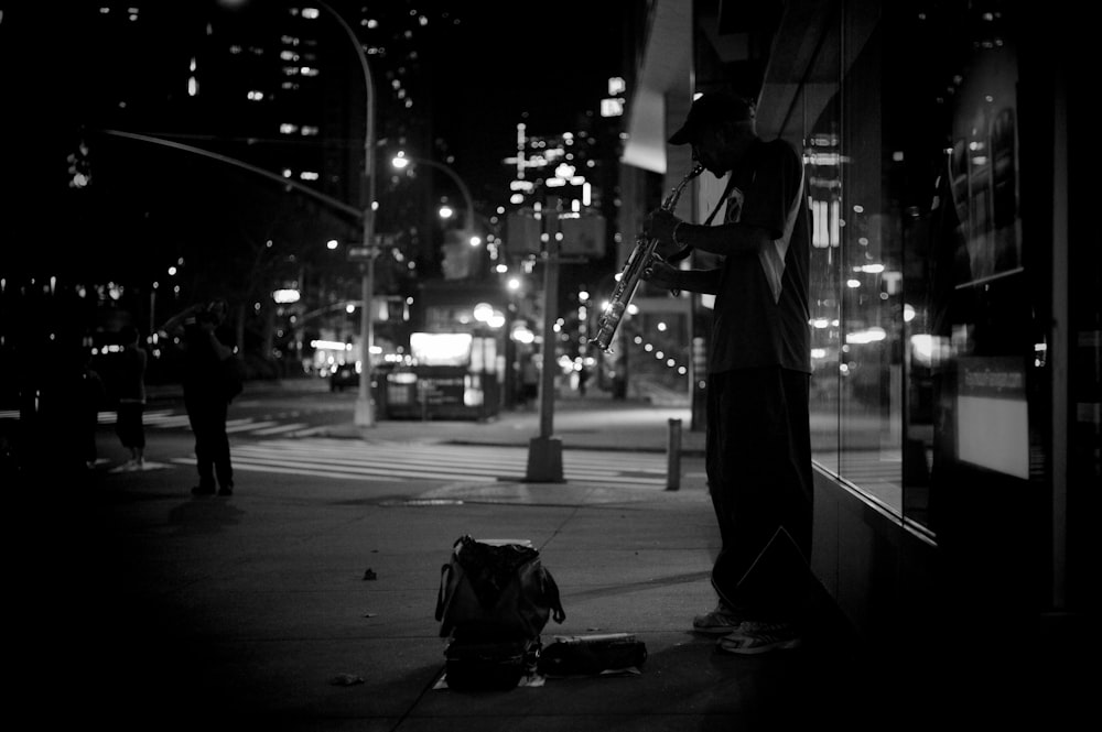 grayscale photography of man playing musical instrument beside road