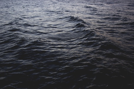 Dark ocean waves ripple across the surface, creating a textured pattern. The lighting gives the water a deep blue-gray color, accentuating the movement of the waves in a serene yet somewhat ominous manner.
