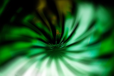 A digital art piece featuring a swirling pattern of green hues that appear to be spiraling towards the center, creating a sense of depth and motion. The darker edges contrast with the lighter center, enhancing the visual effect.