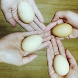 Close-up of hands gently holding fresh eggs against a natural wood background.