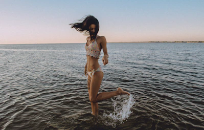 A girl in a bikini flicks her leg up behind her in the water at a beach