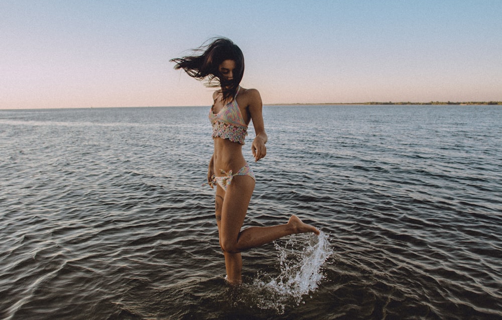 A girl in a bikini flicks her leg up behind her in the water at a beach