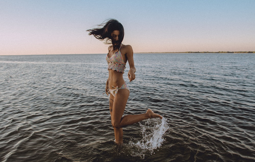 Une fille en bikini lève sa jambe derrière elle dans l’eau d’une plage
