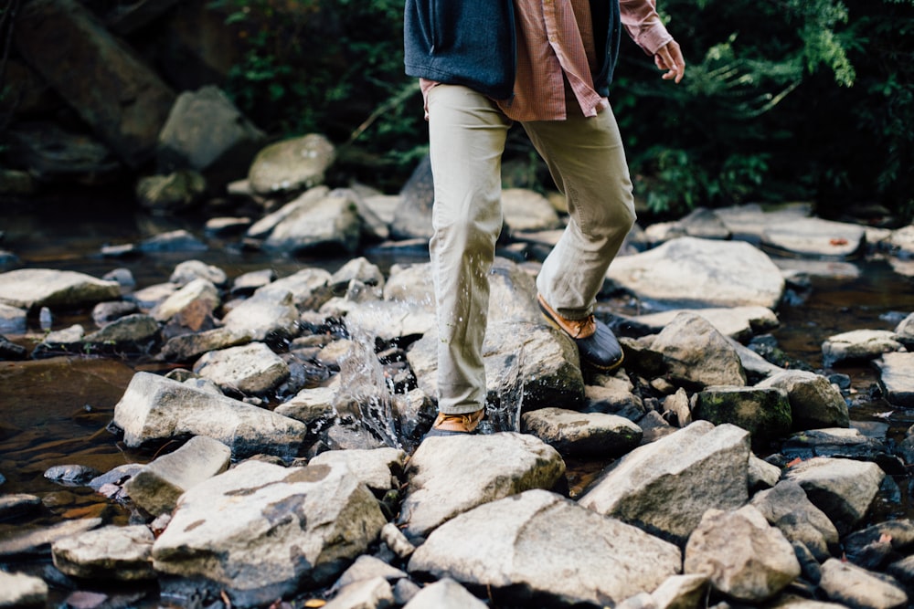 man trekking on gray rocks in body of water at daytime