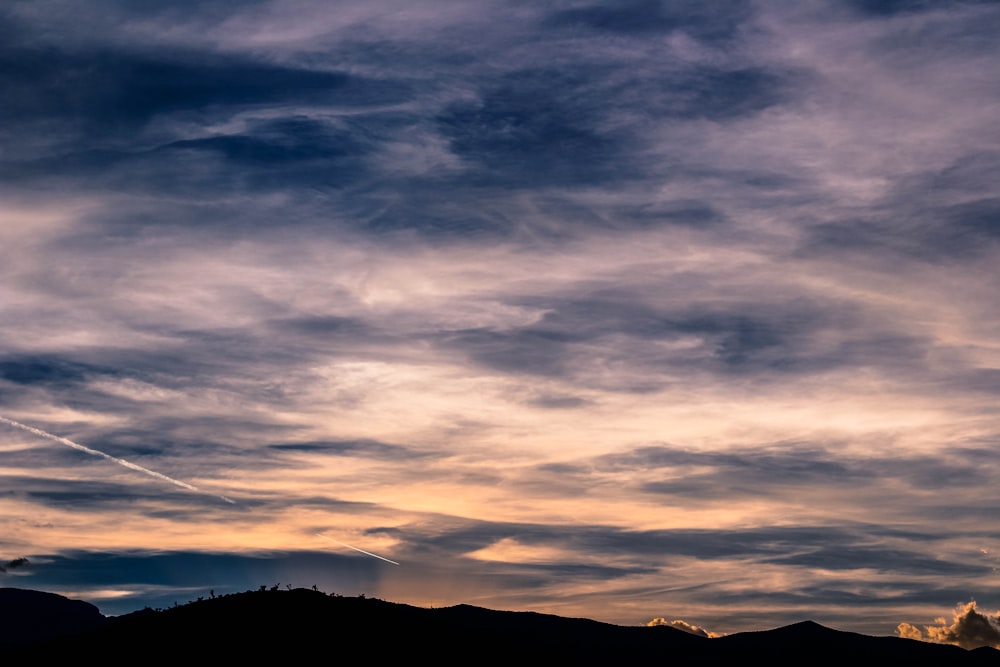 silhouette of mountains under blue and white cludy sky