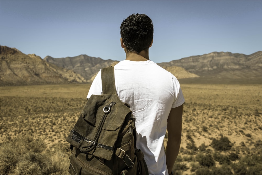 man standing in front dried grass field near gray mountains under gray sky