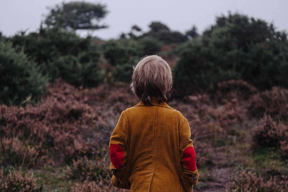 茶色のコートを着た少年が浅い焦点の写真で木々を眺めている