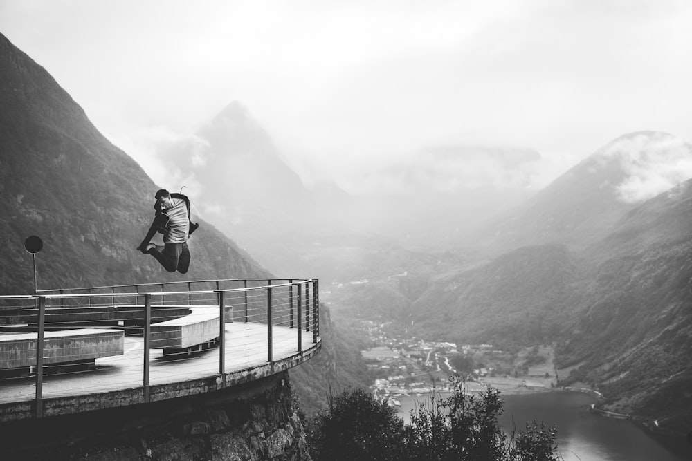 grayscale photo of man jumping near mountains